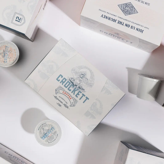 Medium-bodied coffee packaging featuring Crockett Coffee branding with individual pods and boxes arranged on a light background.