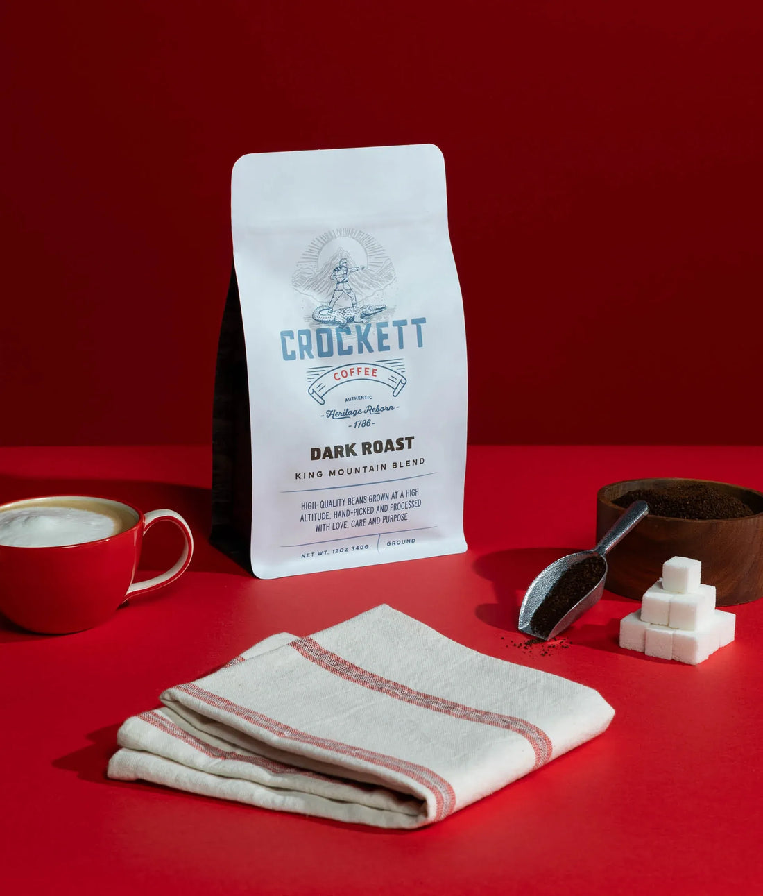 Coffee pods featured alongside a rich dark roast coffee bag, sugar cubes, and a frothy cappuccino on a red background.