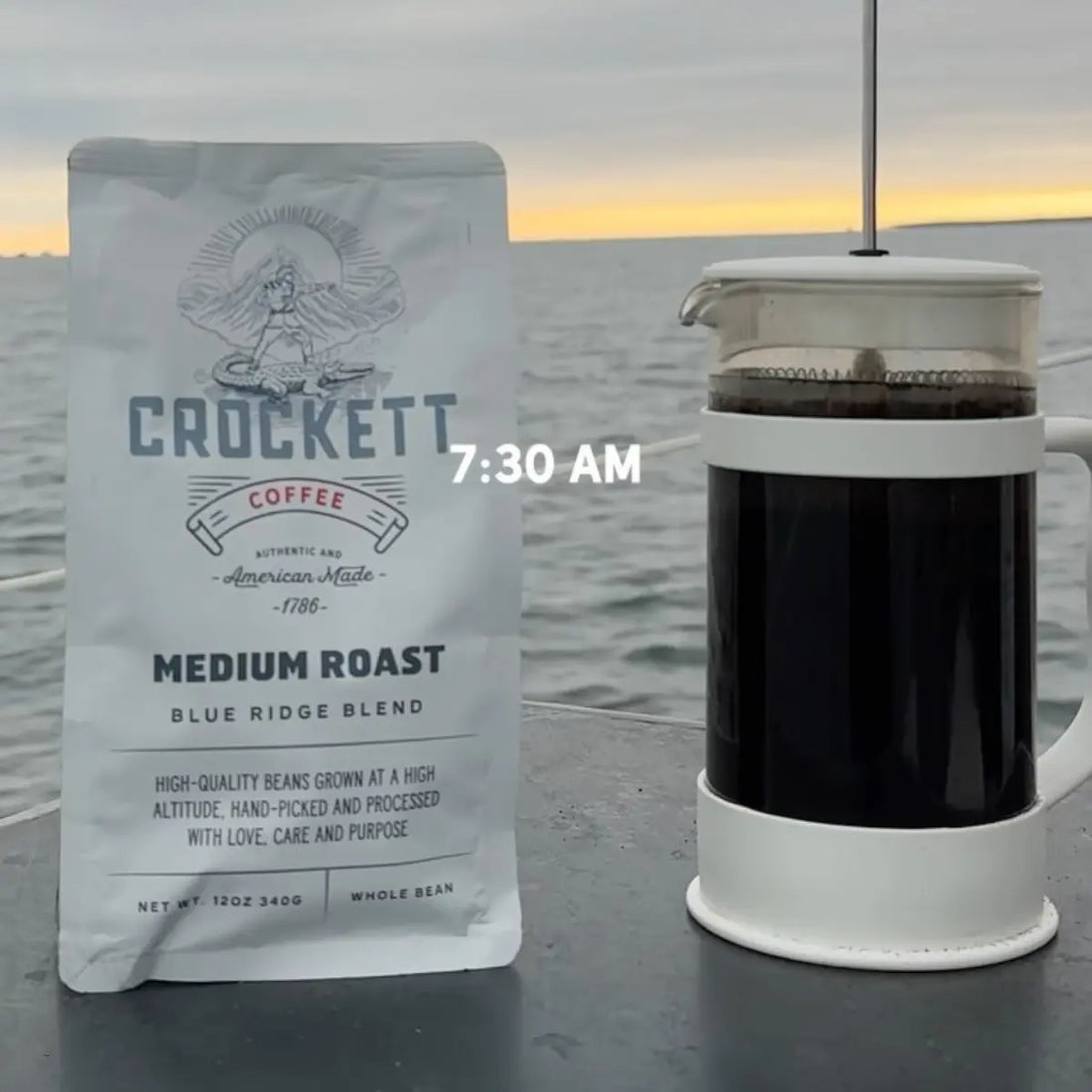 Small batch craft coffee beside a French press on an outdoor table overlooking a calm sea at sunrise