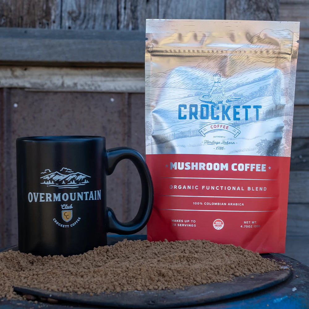 Mushroom coffee being scooped from a Crockett Coffee bag next to a branded white mug.