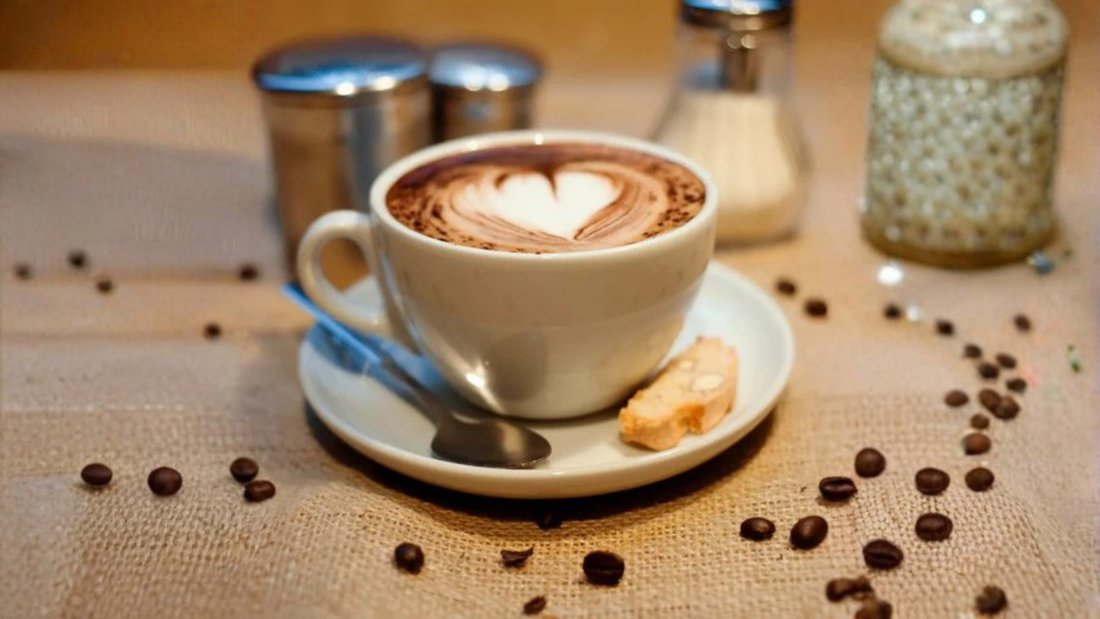 Cappuccino on a table with some spice and sugar shakers in the background.