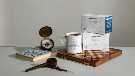 K-Cup coffee in packaging on a chessboard with a full mug of coffee.