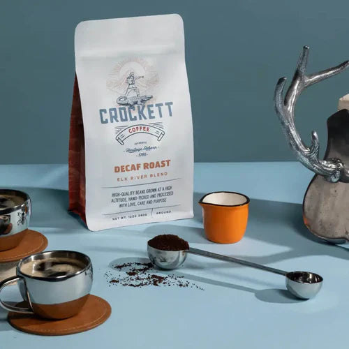 Good decaf coffee featuring Crockett Coffee's decaf roast bag, espresso cups, and a scoop of ground coffee on a blue surface