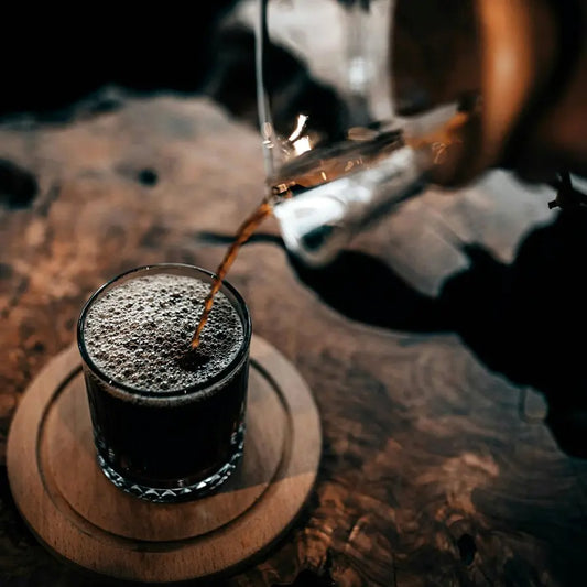 High acid coffee roast poured from a glass carafe into a short tumbler on a rustic wooden table