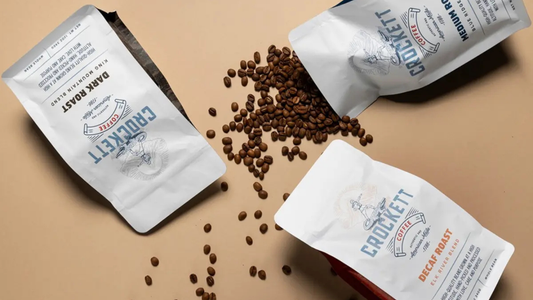 Crockett Coffee whole bean bags laying flat on a surface with coffee beans around them.