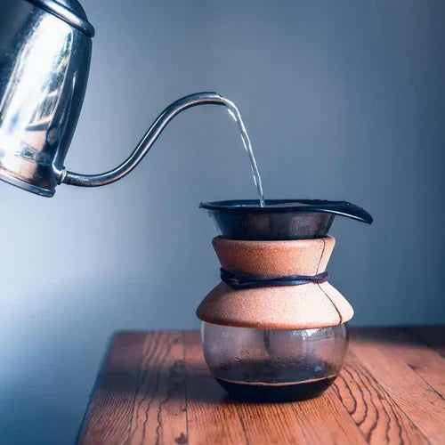 Medium roast coffee being brewed with a pour-over method as hot water flows from a gooseneck kettle into a filter