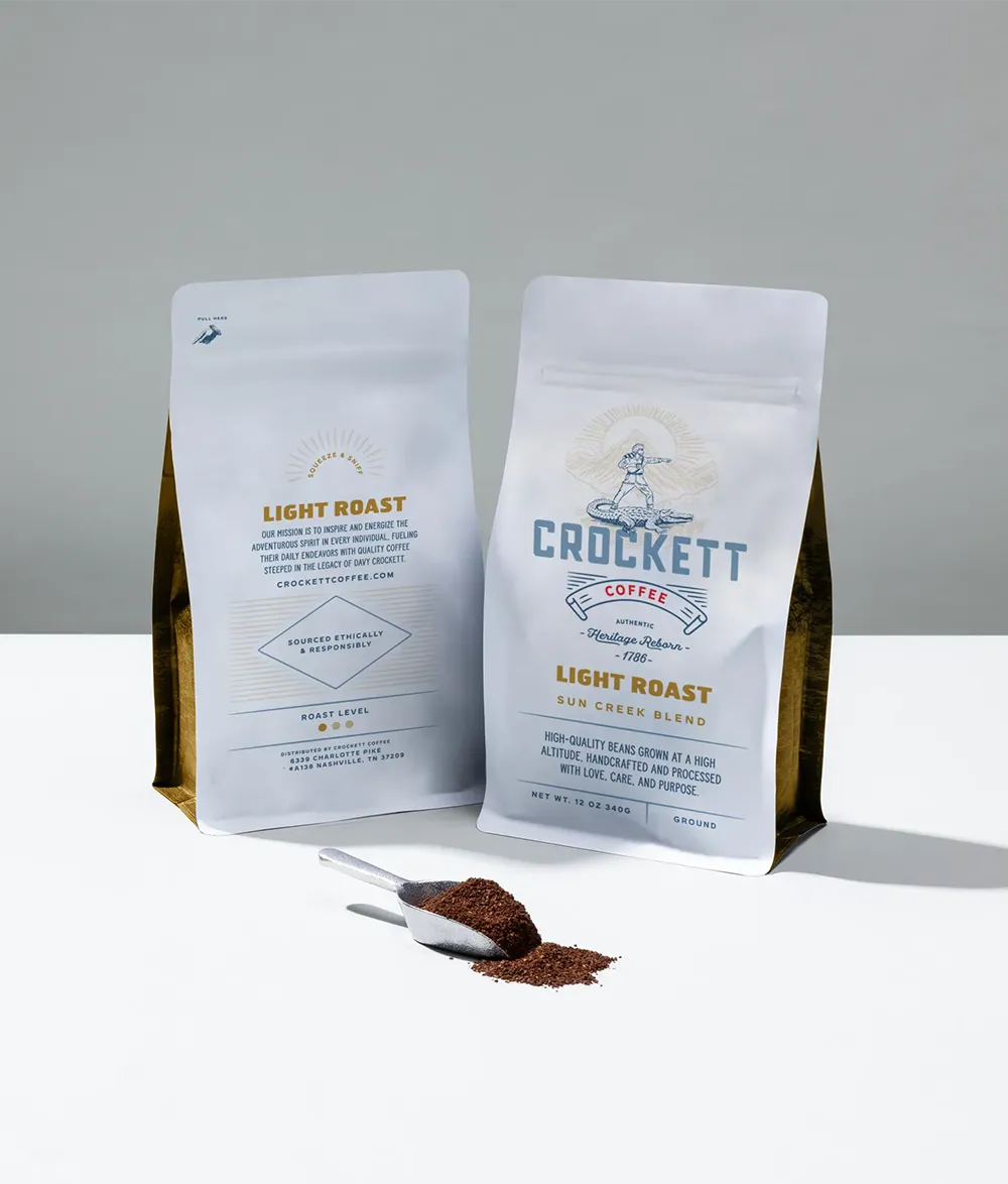 Light roast coffee bags labeled “Sun Creek Blend” from Crockett Coffee, with ground coffee spilling from a scoop in the foreground.