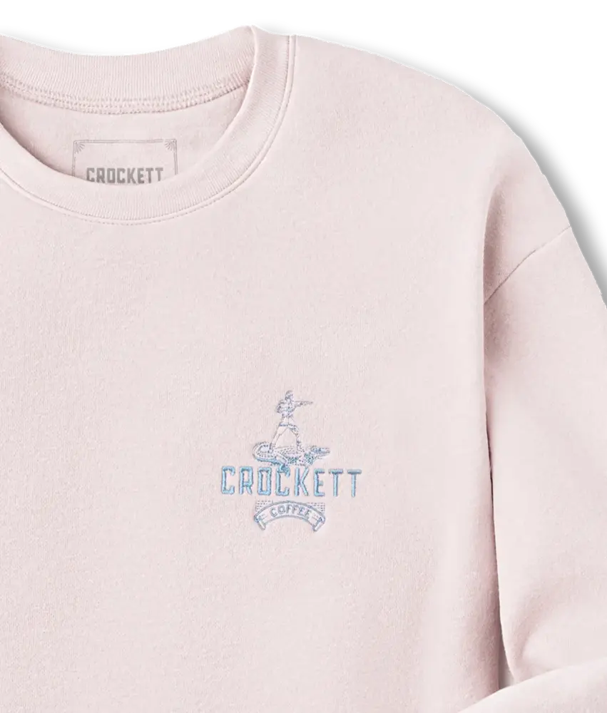 Pale pink sweatshirt with blue embroidered Crockett Coffee logo and figure detail on the left chest.