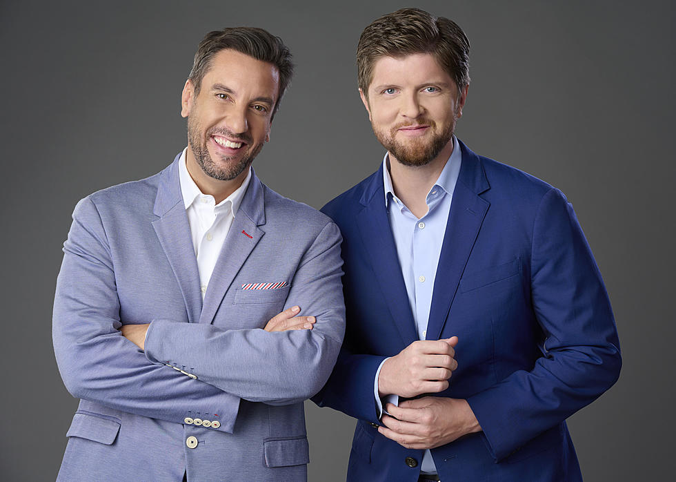 Two men in suits standing side by side against a gray background
